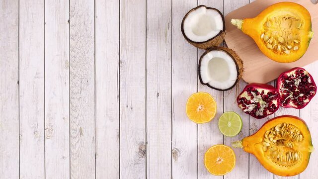 Sliced ripe tropic and citrus fruits appear on right side of light wooden theme. Stop motion 