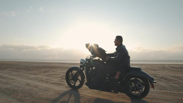Guy with a girl on a motorcycle in the desert. Couple riding on vintage motorcycle and having a good time at sunset on a dry salt lake. Slow motion shot
