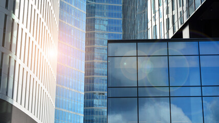 Blue curtain wall made of toned glass and steel constructions under blue sky. A fragment of a building. Glass facades on a bright sunny day with sunbeams in the blue sky.