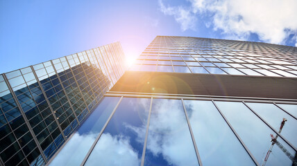 Bottom view of modern office buildings in the business district. Skyscraper glass facades on a bright sunny day with sunbeams in the blue sky.