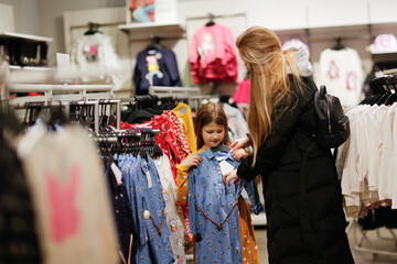 Fototapeta na wymiar Two sisters friends choose a dress in a store, an older sister helps a girl to try on a dress for a child, sibling relationship, joint shopping