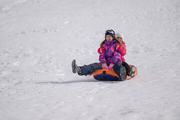 Fototapeta na wymiar two happy active kids delightful girls riding tube on snow slope during winter mountain resort activity with copy space