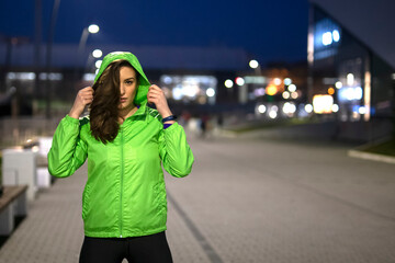 Fototapeta premium Fit woman in sport jacket on the street exercise with ciity lights on background