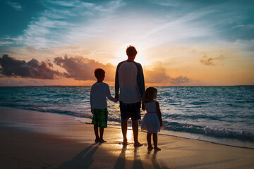 father and two kids walking on beach at sunset