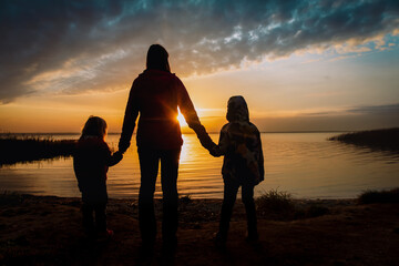 mother with kids looking at sunset on lake, family in nature