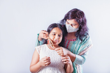Indian mother putting beautiful handmade face mask on her serious daughter