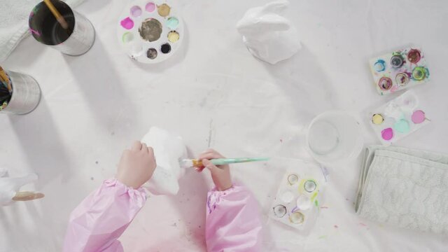 Flat lay. Little girl painting paper mache figurine at homeschooling art class.