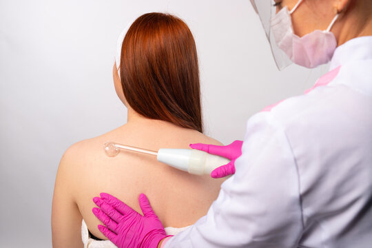 An cosmetologist apply darsonval gently rubbing it all over the back. Health and personal care concept. Photo on white background