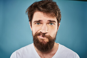 Fototapeta premium Bearded man displeased facial expression emotions close-up blue background white t-shirt