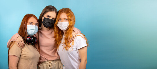 Banner, long format. Social distance. Three girlfriends hugged each other, but they also wear masks against the spread of the virus for the pandemic. Photo on blue background with large side space