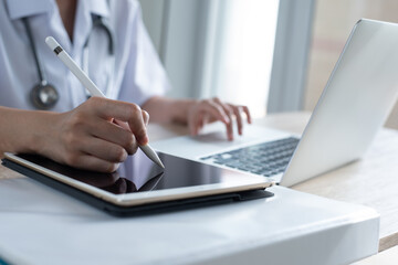 Doctor recording medical report working on digital tablet and laptop computer in medical office