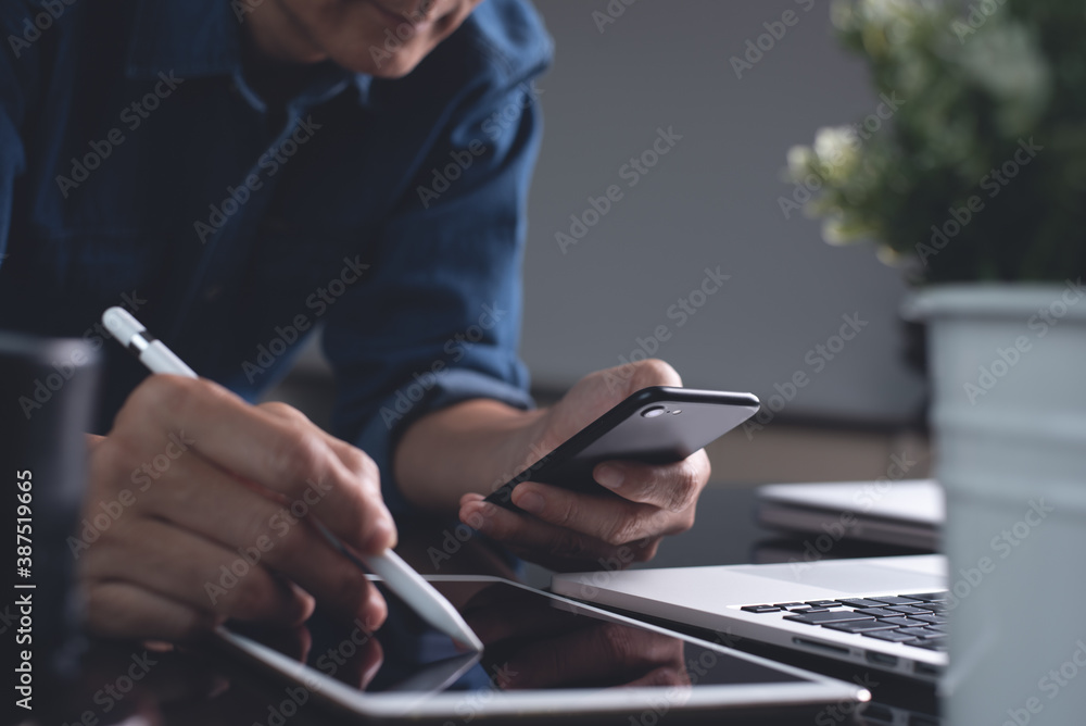 Poster man using mobile phone and digital tablet during working on laptop computer in office