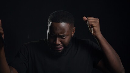 Friendly guy doing movements on black background. Man making gestures indoors