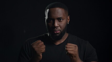 Anxious man warming up hands on black background. Afro guy screaming indoors