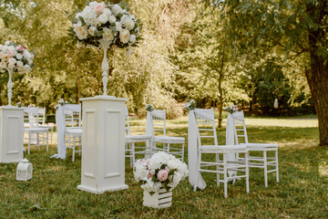 Wedding ceremony outdoors in the park. White chairs decorated with roses.