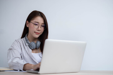 Young Asian woman wearing headphones to study online with her teacher, the girl is happy to learn, listen to the lecture inside the coffee shop on a white background.