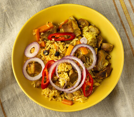 Asian pilaf in a yellow teatka on a napkin with onion rings and red hot pepper. Close up. Top view
