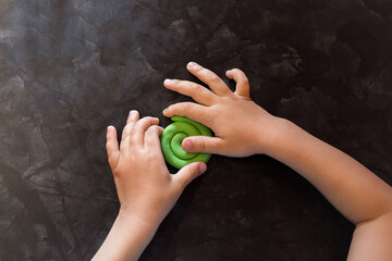 a child's hands on a black table blinded a green plasticine snail. Image with selective focus and noise effect