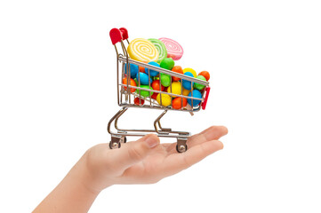 Child's hand holding shopping cart with lollipops and sweet dragee. Isolated on white.