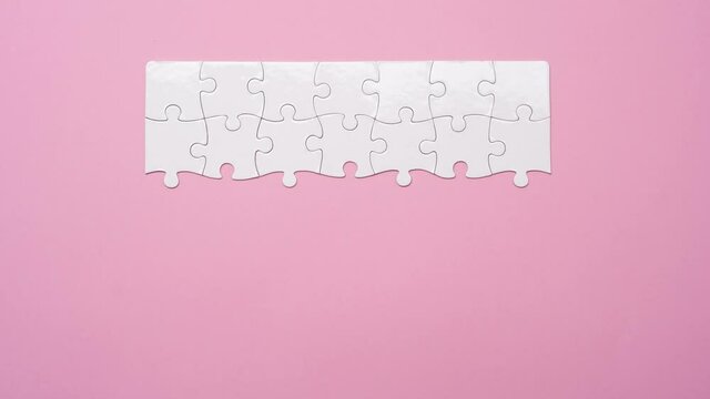 Top view of matching white rectangular jigsaw puzzle pieces on pink background, timelapse