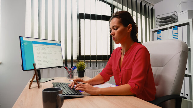 Hispanic Young Woman Sitting In Office And Working On Desktop Pc. Entrepreneur Sitting In Front Of Computer In Professional Company Workspace Typing On Keyboard Looking At Monitor Writing Reports