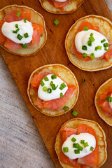 Homemade Blini with Smoked Salmon, Creme and Chives on a rustic wooden board, top view. Close-up.