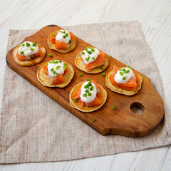 Homemade Blini with Smoked Salmon, Creme and Chives on a rustic wooden board, side view.