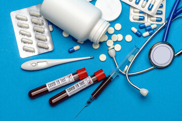 Stethoscope, syringe, thermometer, blood test tube and can of pills on blue background top view with copy space