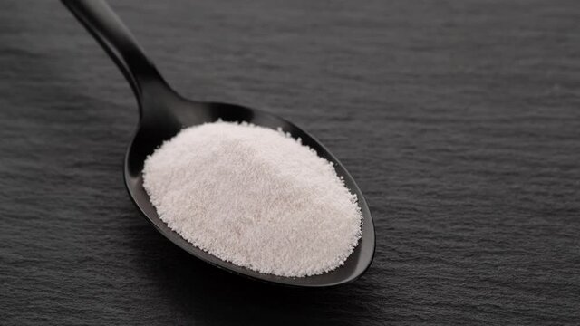 collagen powder peptide in black spoon on black stone. Natural beauty and health supplement top view
