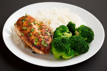 Homemade Chicken Breast, Rice and Broccoli on a white plate on a black background, low angle view.