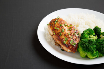 Homemade Chicken Breast, Rice and Broccoli on a white plate on a black surface, side view. Space for text.