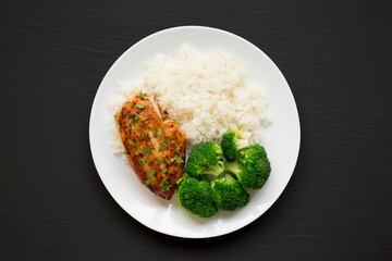 Homemade Chicken Breast, Rice and Broccoli on a white plate on a black surface, top view. Flat lay, overhead, from above.