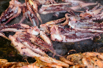 Octopus cooked on a black grill at a street food festival, ready to eat seafood, side view.