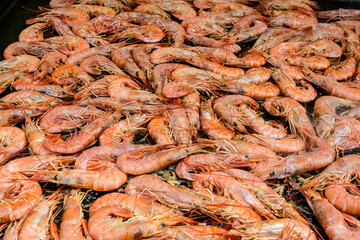 Close up of large portion of cooked shrimps with tomato sauce and yellow lemons in a large pan at a street food festival, ready to eat healthy seafood, beautiful orange monochrome outdoor background.