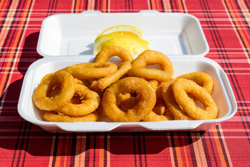 Large group of freshly fried calamari and onion rings on display for sale at a street food festival, ready to eat healthy seafood, beautiful orange monochrome outdoor background.