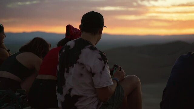 Happy group of friends enjoying a colorful sunset at a desert, in The great sand dunes national park, in Colorado, USA - handheld shot