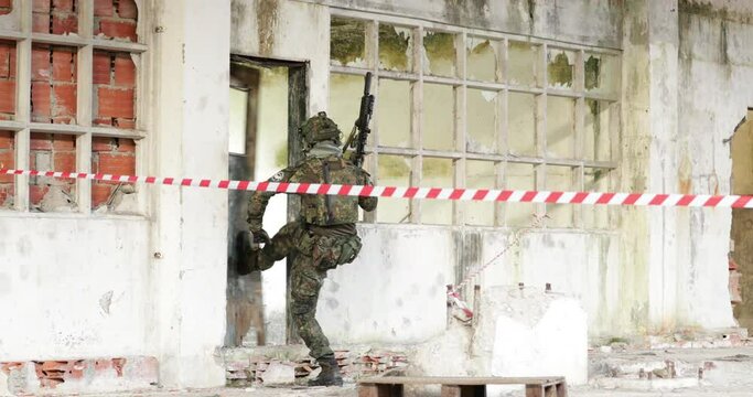 Airsoft Player On Camouflage Uniform And Holding A Rifle Gun Kicks The Door For Him To Enter.  - wide shot