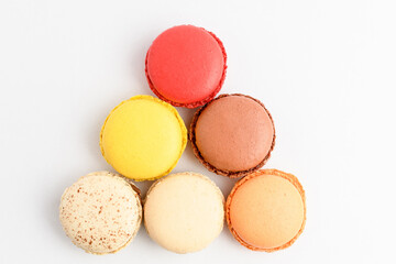 Top view of six sweet French macarons isolated on white background, flavours of lemon, orange, strawberry, coconut, vanilla and chocolate, pastel colors.