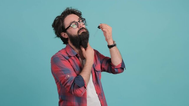 Close up of a bearded man applies his beard care oil, isolated on a turquoise background. Hair care concept.