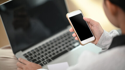 Cropped shot of a young female working with mock up laptop while looking an information on mock up smartphone.