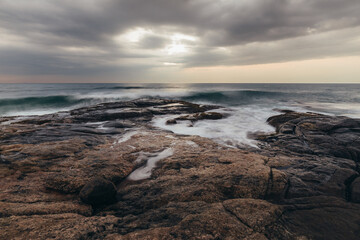 Fototapeta na wymiar Waves breaks textured rocky ocean coast under dramatic cloudy sky on Sri Lanka island.