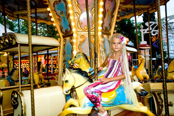 The little girl rides a carousel. Amusement park.