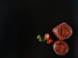 ketchup in glass jars and tomatoes on a black background 