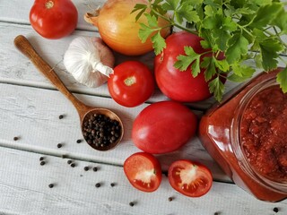 homemade delicious ketchup in a glass jar and its organic ingredients on a white table 