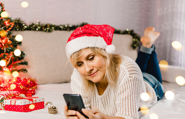 Christmas online shopping. Female buyer makes order on mobile phone. Woman buy presents, prepare to xmas, gift box in hand.