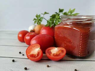 homemade delicious ketchup in a glass jar and its organic ingredients on a white table 