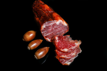 Acorn-fed Iberian loin with three slices cut, garnished with three acorns and with a black background