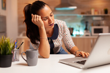 Overworked woman falling asleep in home kitchen late at night. Employee using modern technology at...