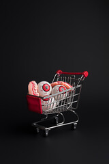 Creative layout made with eyeballs in shopping cart on black background. Minimal Halloween shopping...