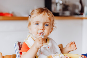 Toddler girl eating cake with a fork in kitchen